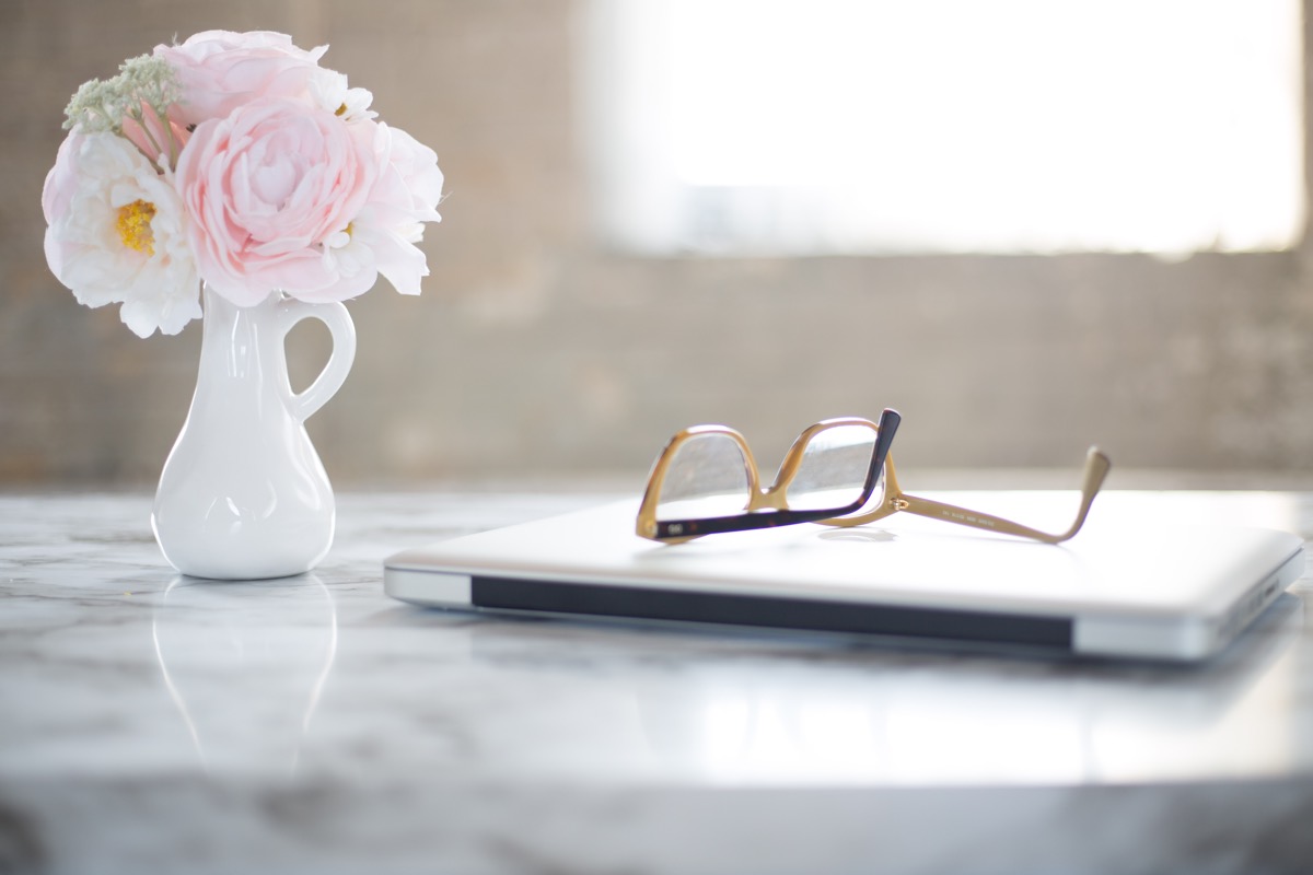 closed laptop computer on desk with flowers and glasses