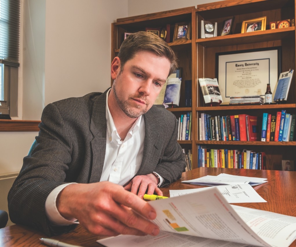 White man in a blazer reading papers at a desk