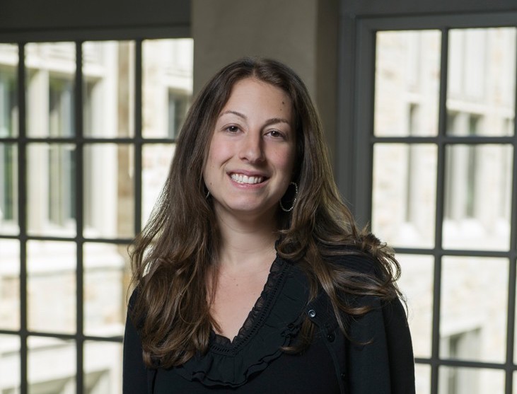 Smiling woman with long brown hair, standing in front of window