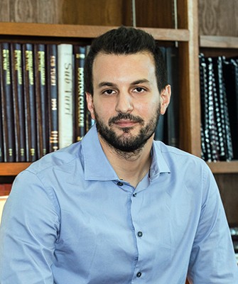 Headshot of man in blue oxford shirt with dark hair and short beard