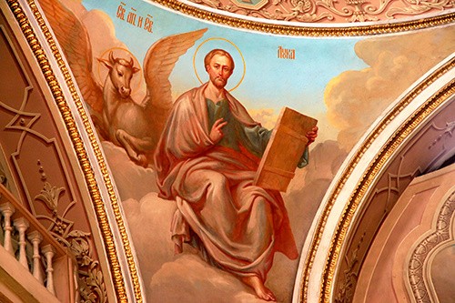 Ceiling painting of St. Luke with a writing surface sitting in clouds with a winged-bull behind him.