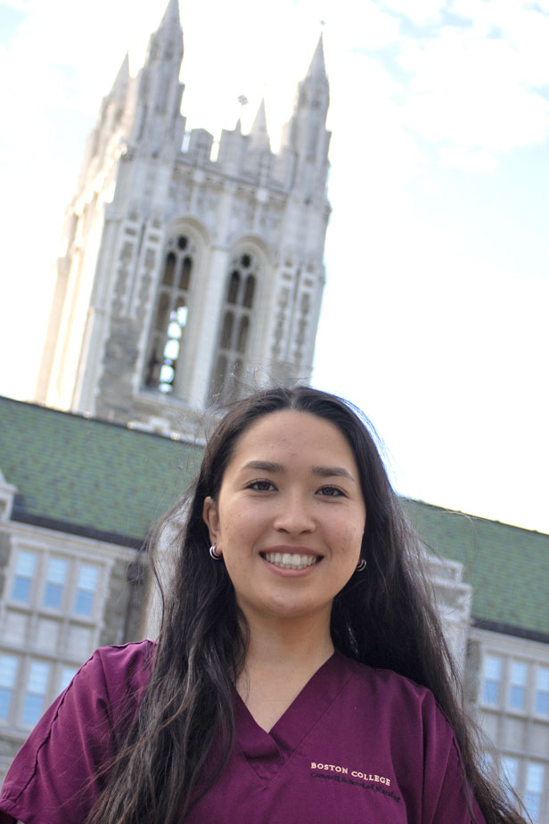 May Tadano in maroon scrubs in front of BC's Gasson Hall
