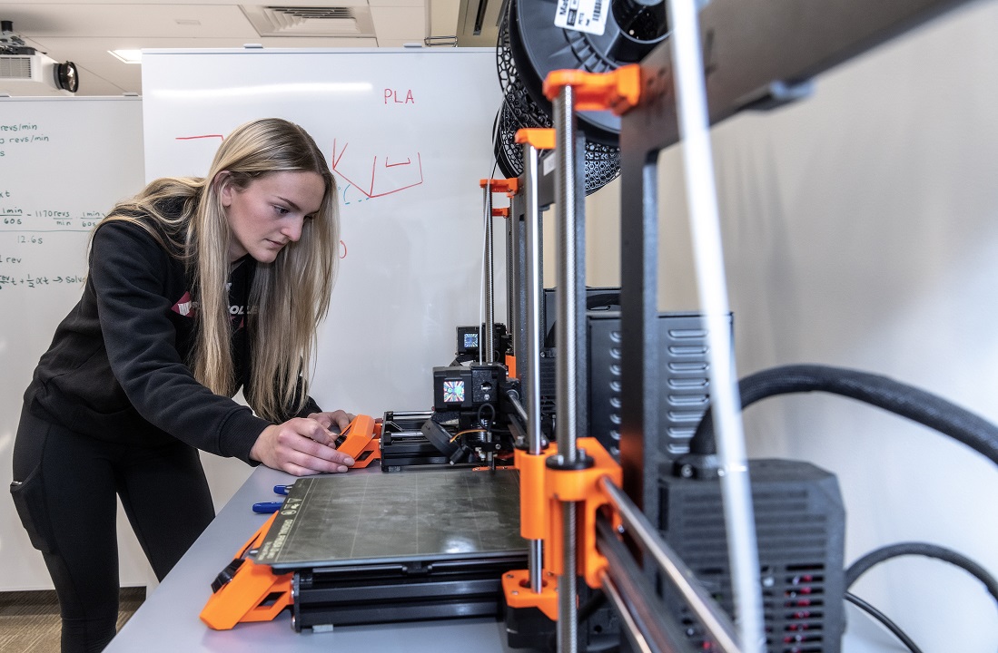 Photoshoot of Ashley Waldron '26 (MCAS) in the Service Building annex of 245 Beacon St. showing the 3D printer that was the equipment that was used to form Ashley's hockey invention.