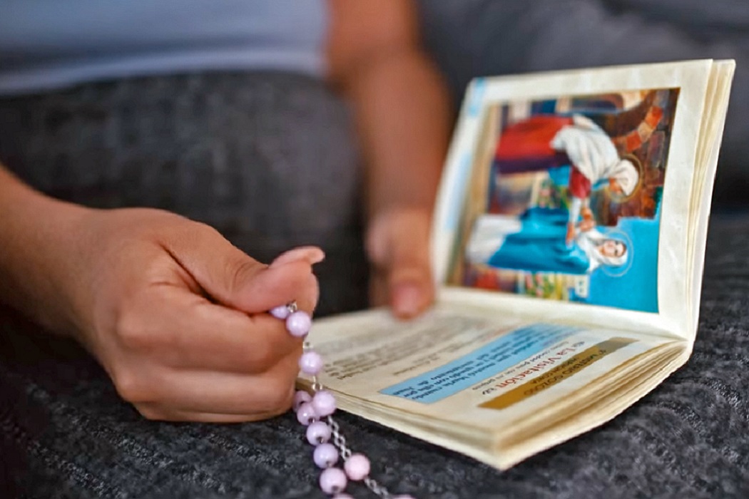 hands holding rosary and prayer book